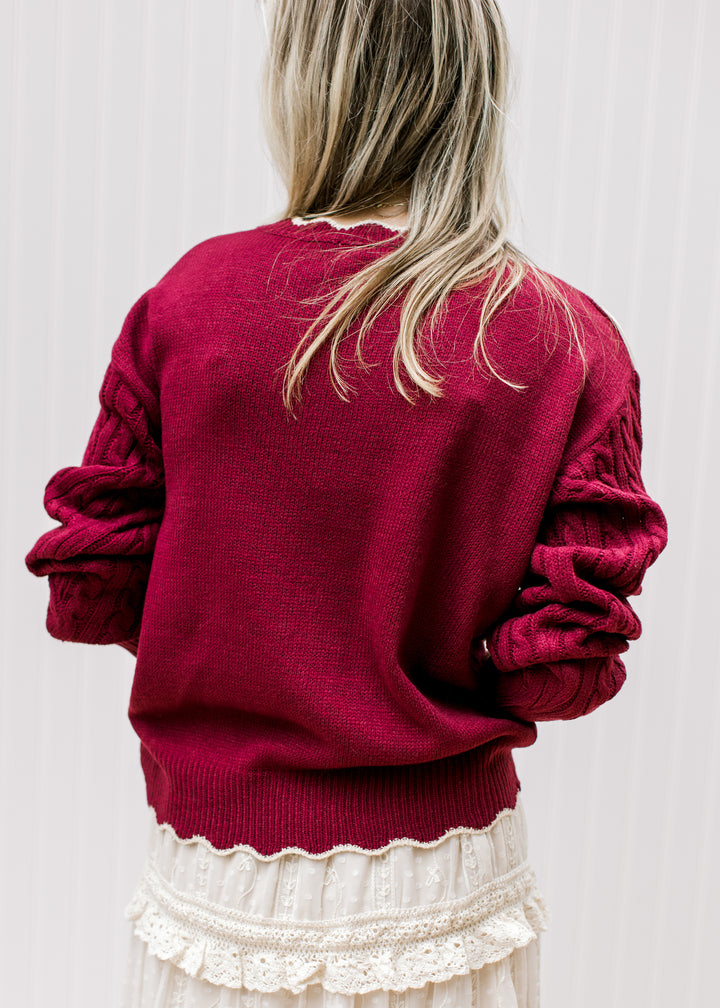 Back view of Model wearing a burgundy long sleeve sweater with cream floral and scalloping. 