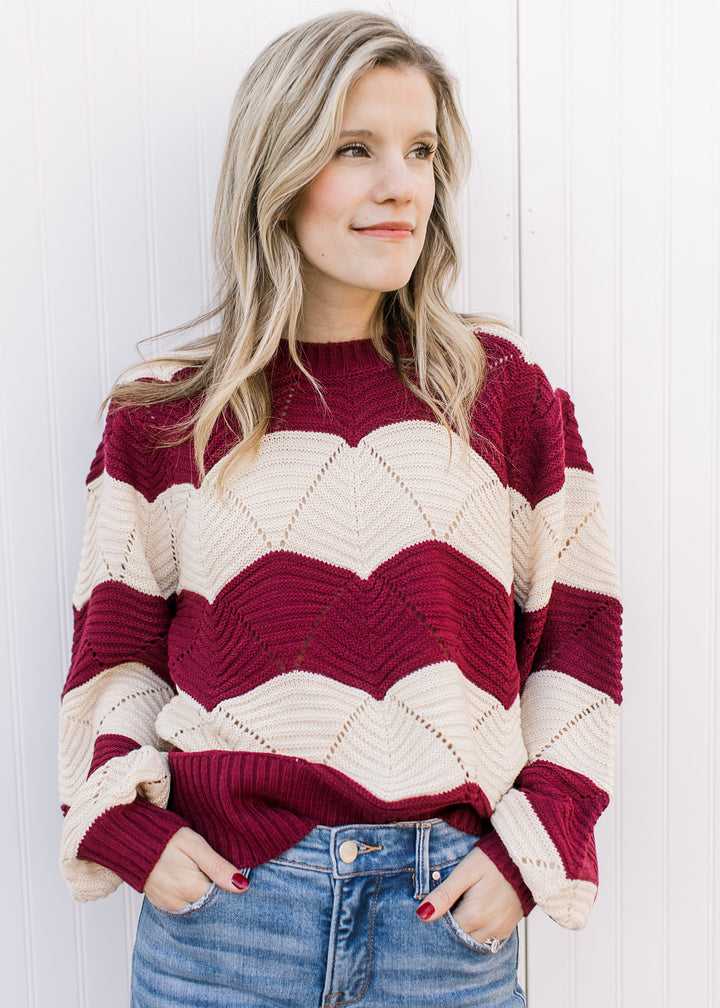 Model wearing a long sleeve cream and burgundy sweater with scalloped stripes and eyelet detailing. 