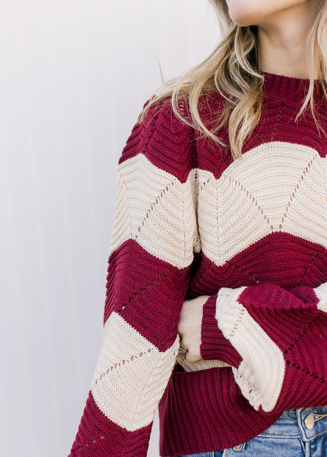 Close up of eyelet detailing throughout a cream and burgundy sweater with scalloped stripes. 