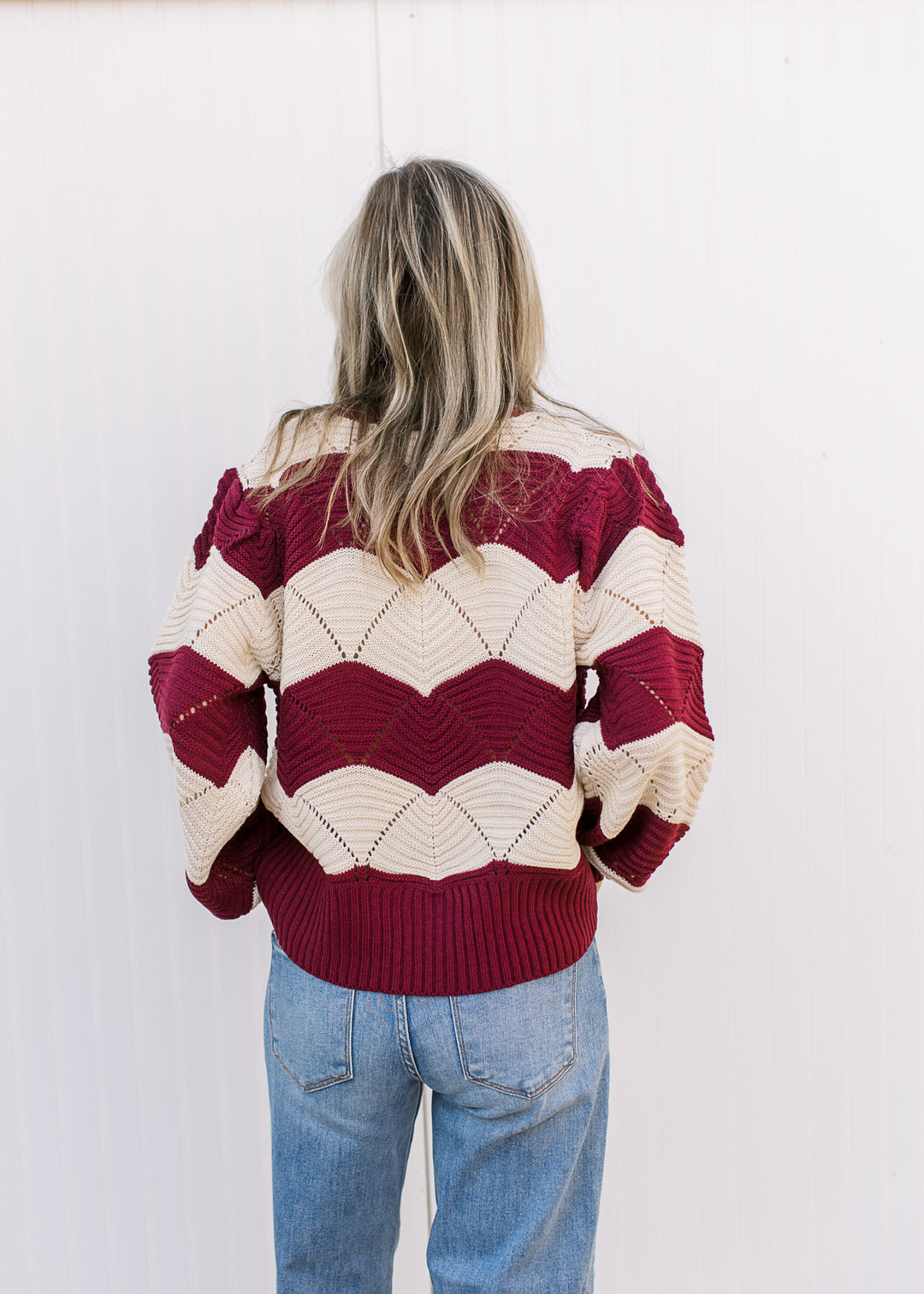 Back view of Model wearing a long sleeve cream and burgundy sweater with scalloped stripes. 