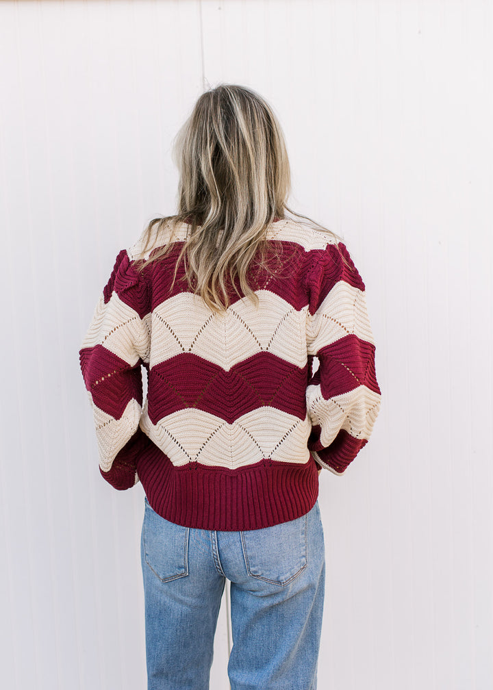 Back view of Model wearing a long sleeve cream and burgundy sweater with scalloped stripes. 
