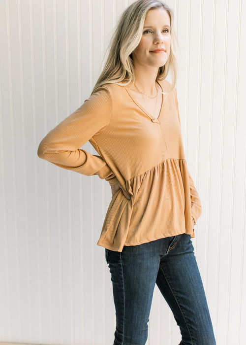 Model wearing a ribbed butterscotch colored top with long sleeves, a v-neck and a babydoll fit.