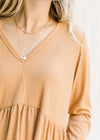 Close up of v-neck and ribbed detailing on a v-neck butterscotch babydoll top with long sleeves. 