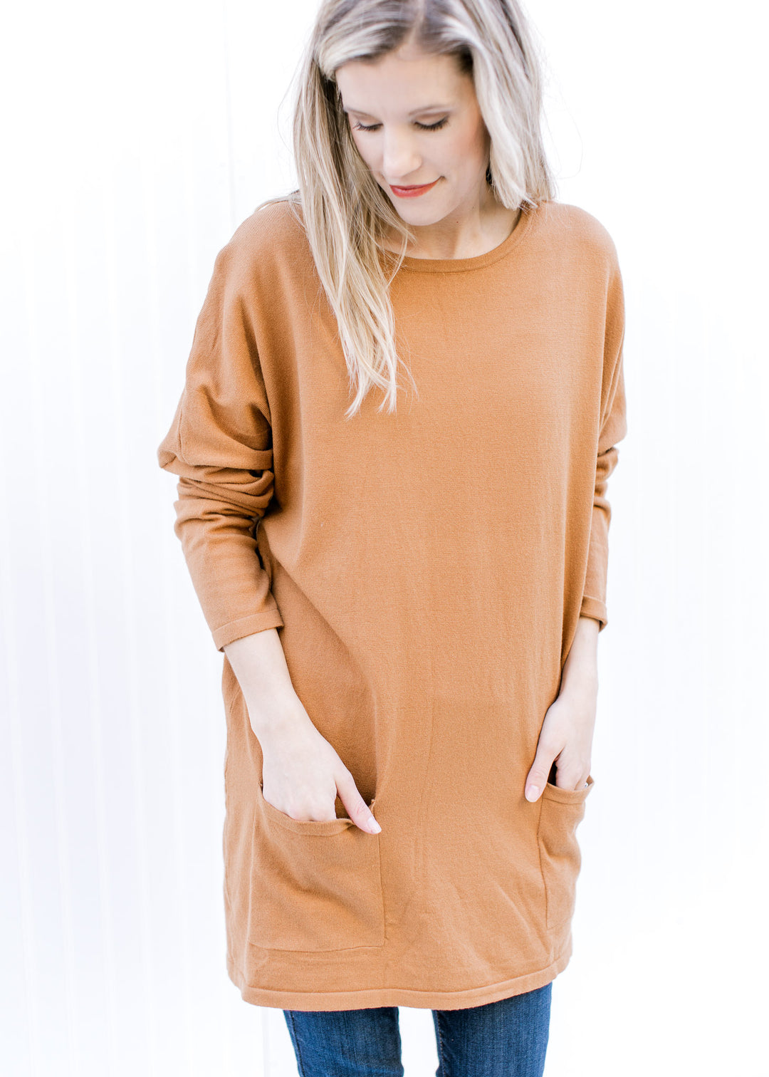 Model wearing jeans and a deep caramel colored tunic with patch pockets and long sleeves. 