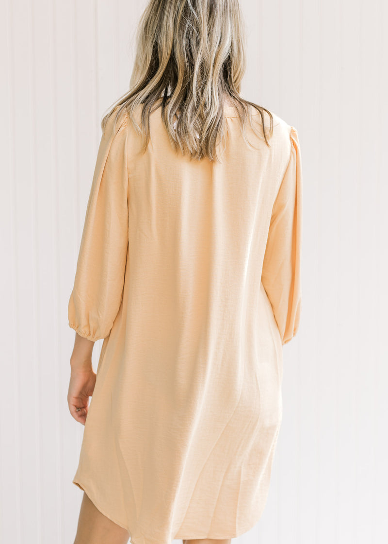 Back view of Model wearing an above the knee dress with a straw color and 3/4 bubble sleeves.
