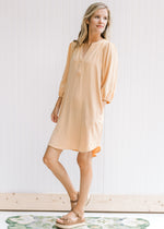 Model wearing sandals with a v-neck dress with a straw color and 3/4 bubble sleeves. 