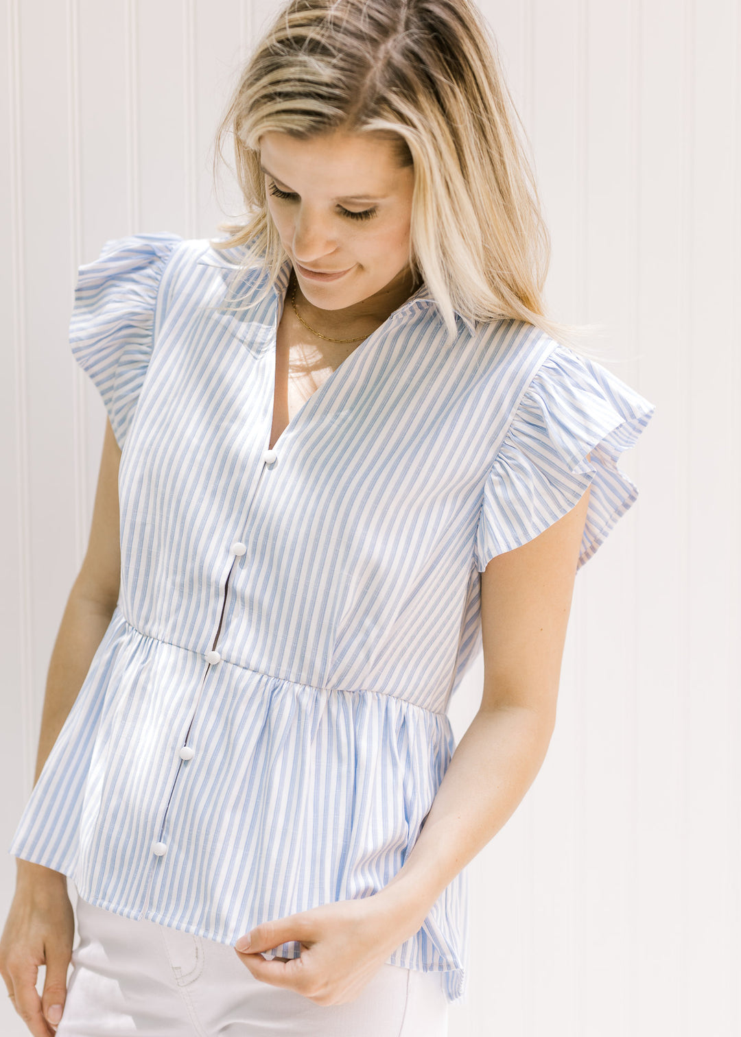 Model wearing a lightweight blue and white striped button up, v-neck top with ruffle short sleeves.