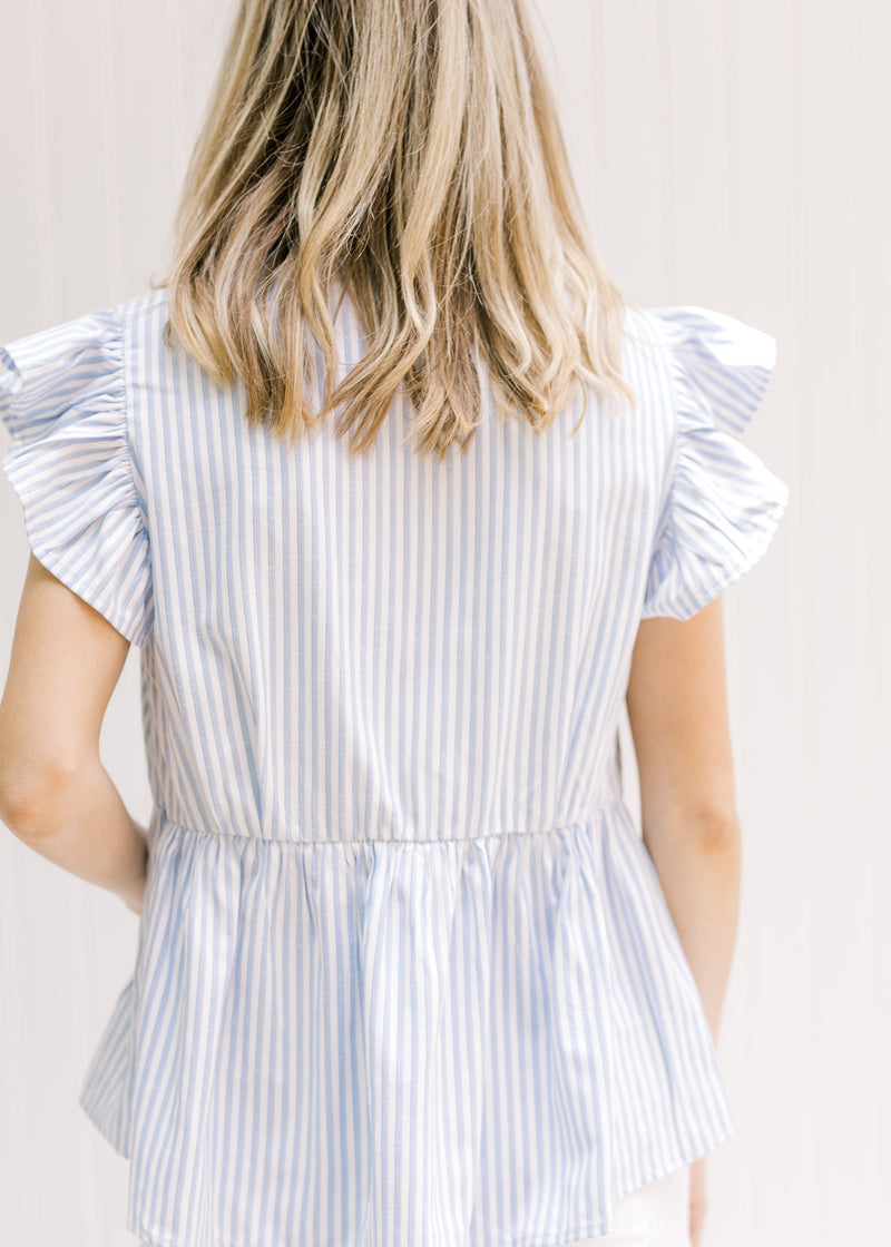 Back view of Model wearing a lightweight blue and white striped top with ruffle short sleeves.