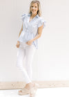 Model wearing white pants with a blue and white striped button up top with ruffle short sleeves.