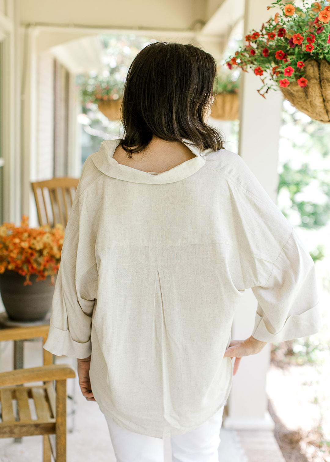 Back view of Model wearing an oatmeal top with a collar, cuffed 3/4 sleeves and a high-low hem.