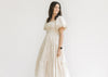 Model wearing a champagne tiered midi with bubble short sleeves and a square neck. 