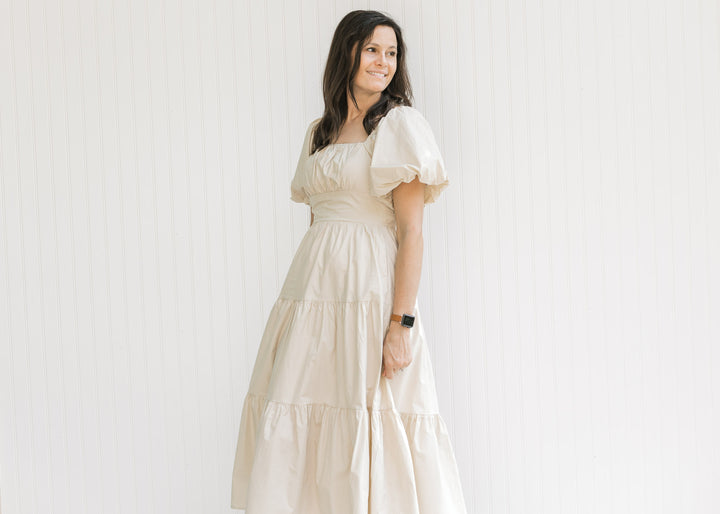 Model wearing a champagne tiered midi with bubble short sleeves and a square neck. 