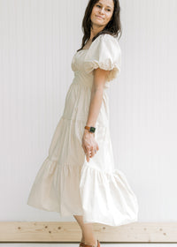 Model wearing a tiered champagne midi dress with short puff sleeves and a smocked back. 
