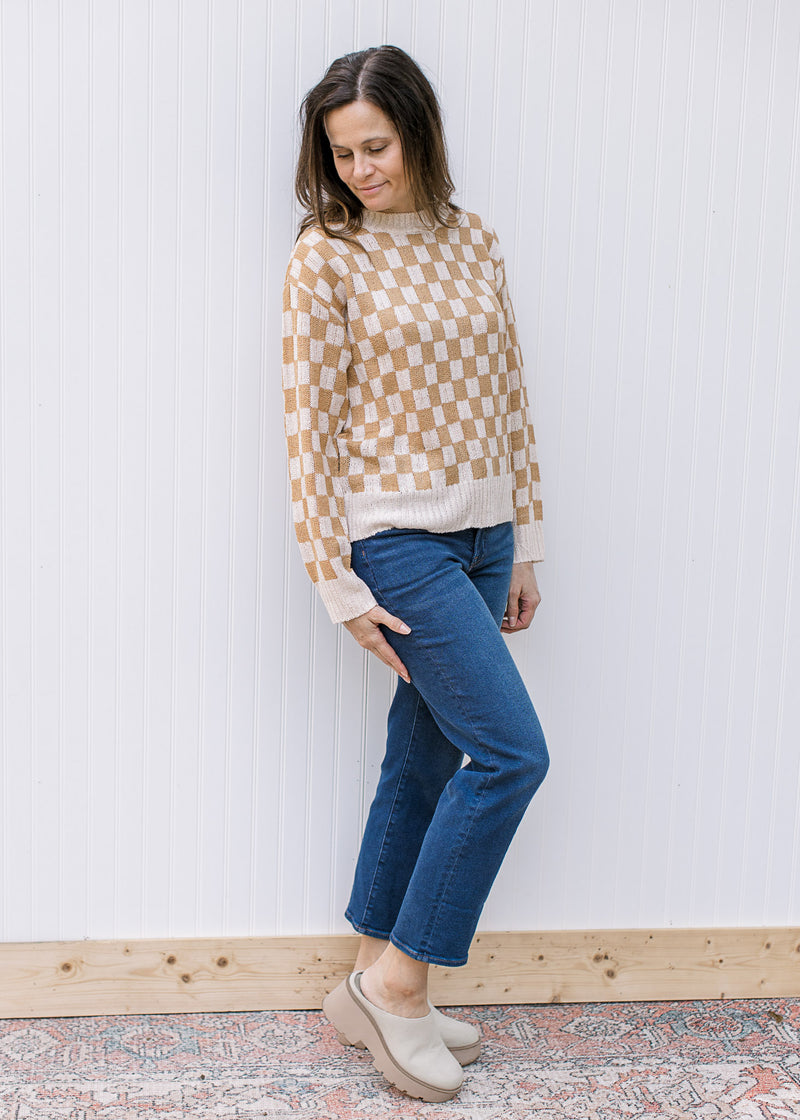 Model wearing jeans with a cream and camel checked sweater with long sleeves.