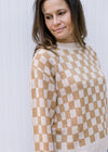 Close up of Model wearing a cream and camel checked sweater with long sleeves and round neck.