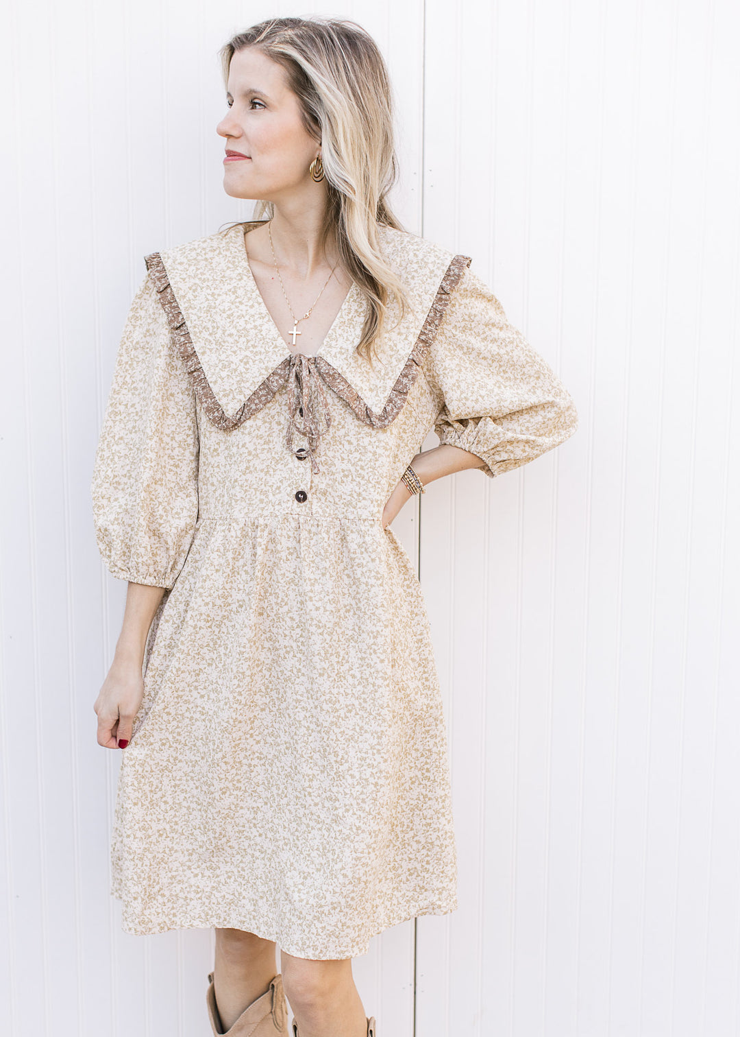 Model wearing a cream dress with taupe floral microprint, 3/4 sleeves and a wide v-neck collar.