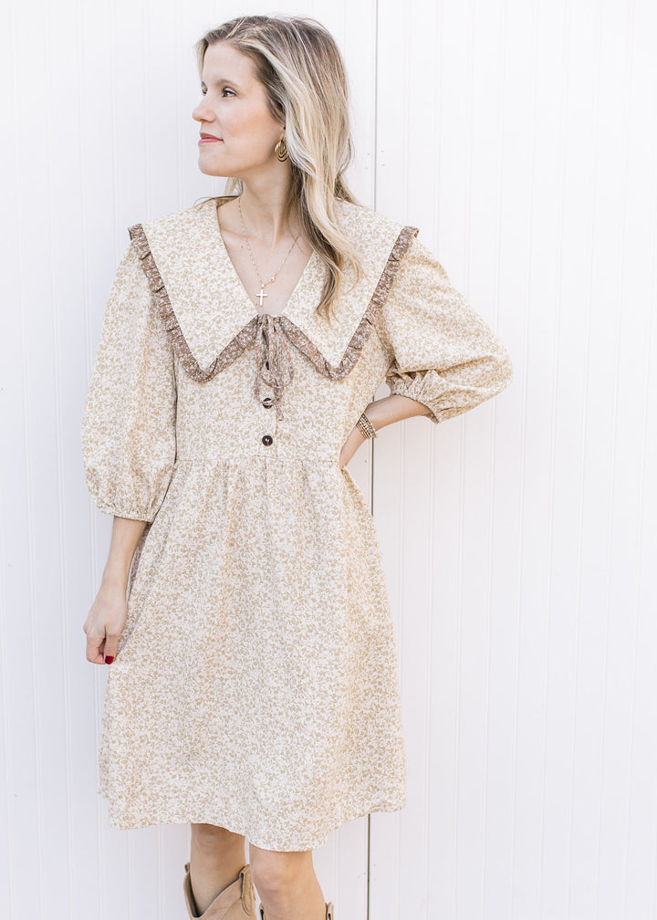 Model wearing a cream dress with taupe floral microprint, 3/4 sleeves and a wide v-neck collar.