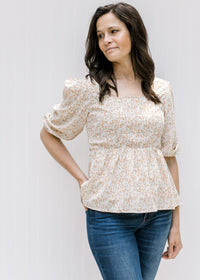 Model wearing a white square neck top with a camel colored floral pattern and a smocked bodice. 