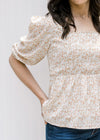 Model wearing a white top with a camel floral pattern, square neckline and 3/4 bubble sleeves. 