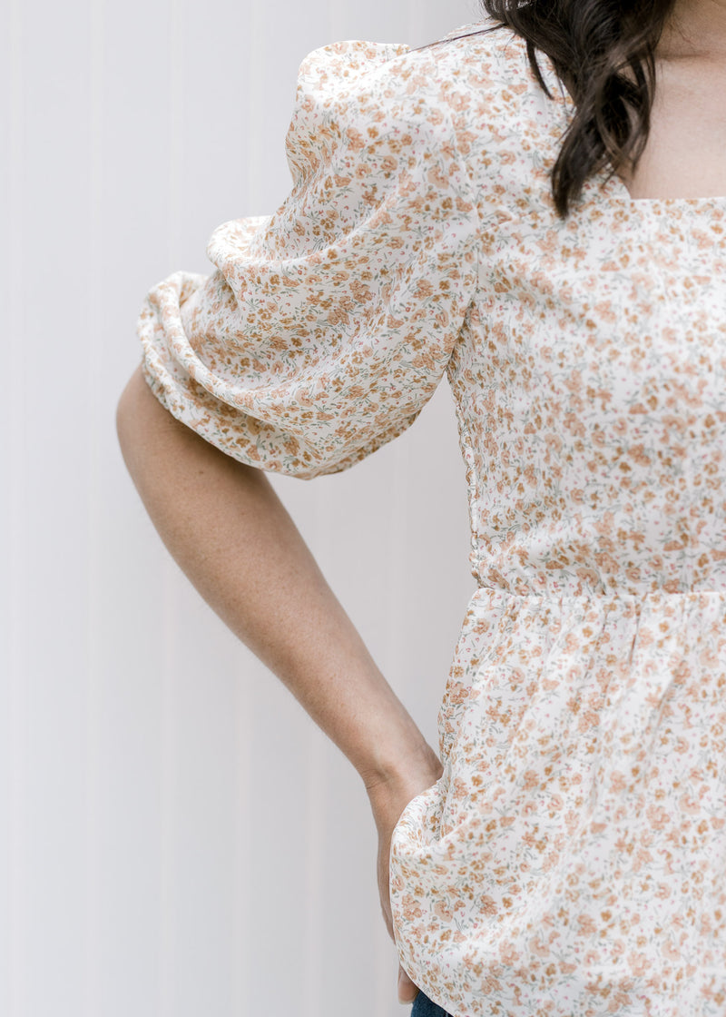 Close up of 3/4 bubble sleeve on a white top with a camel floral pattern and a square neckline. 