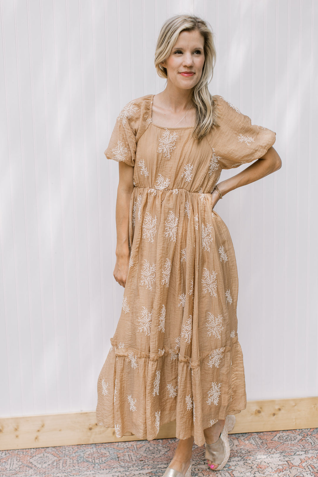 Model wearing a camel dress with white embroidered flowers, elastic wasit and bubble short sleeves.