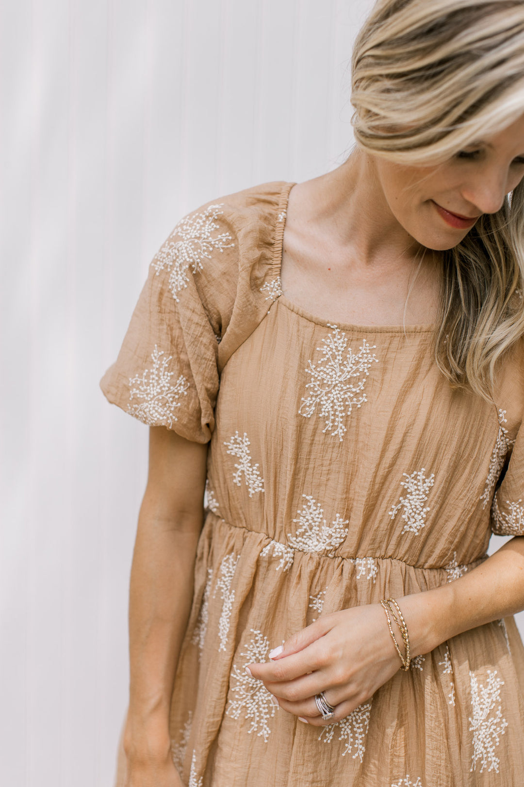 Close up of square neck, bubble short sleeves and elastic band on a camel dress with white flowers.