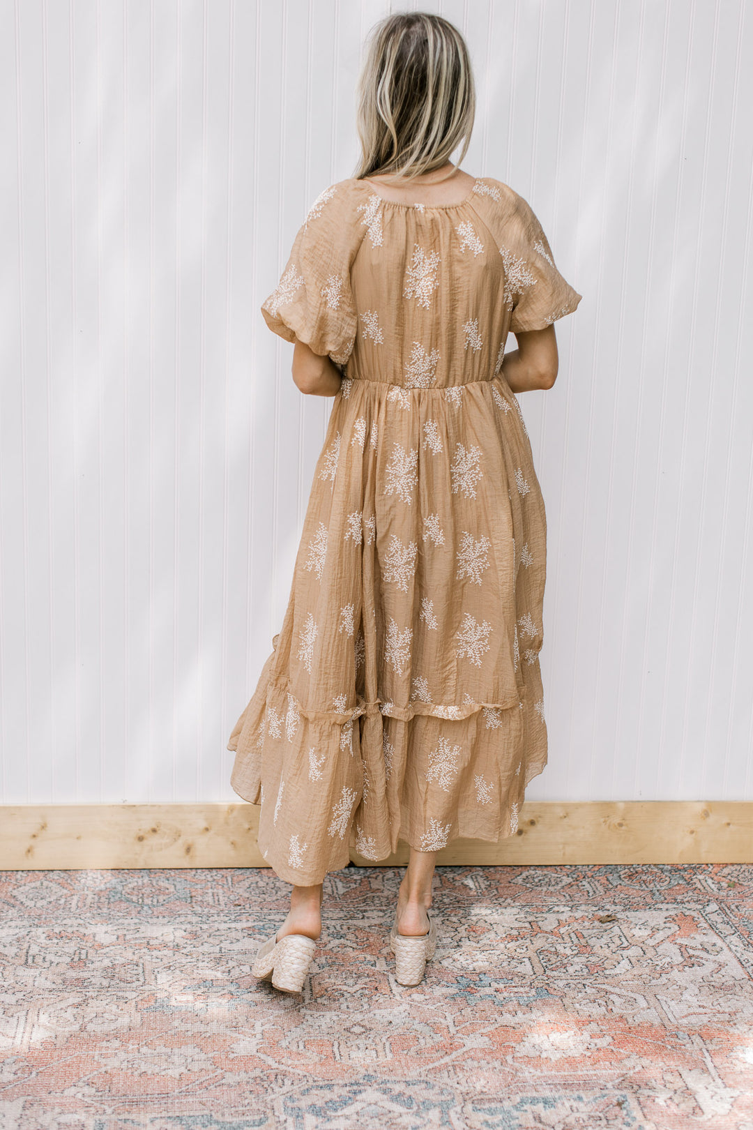 Back view of Model wearing a camel dress with white flowers  and bubble short sleeves.