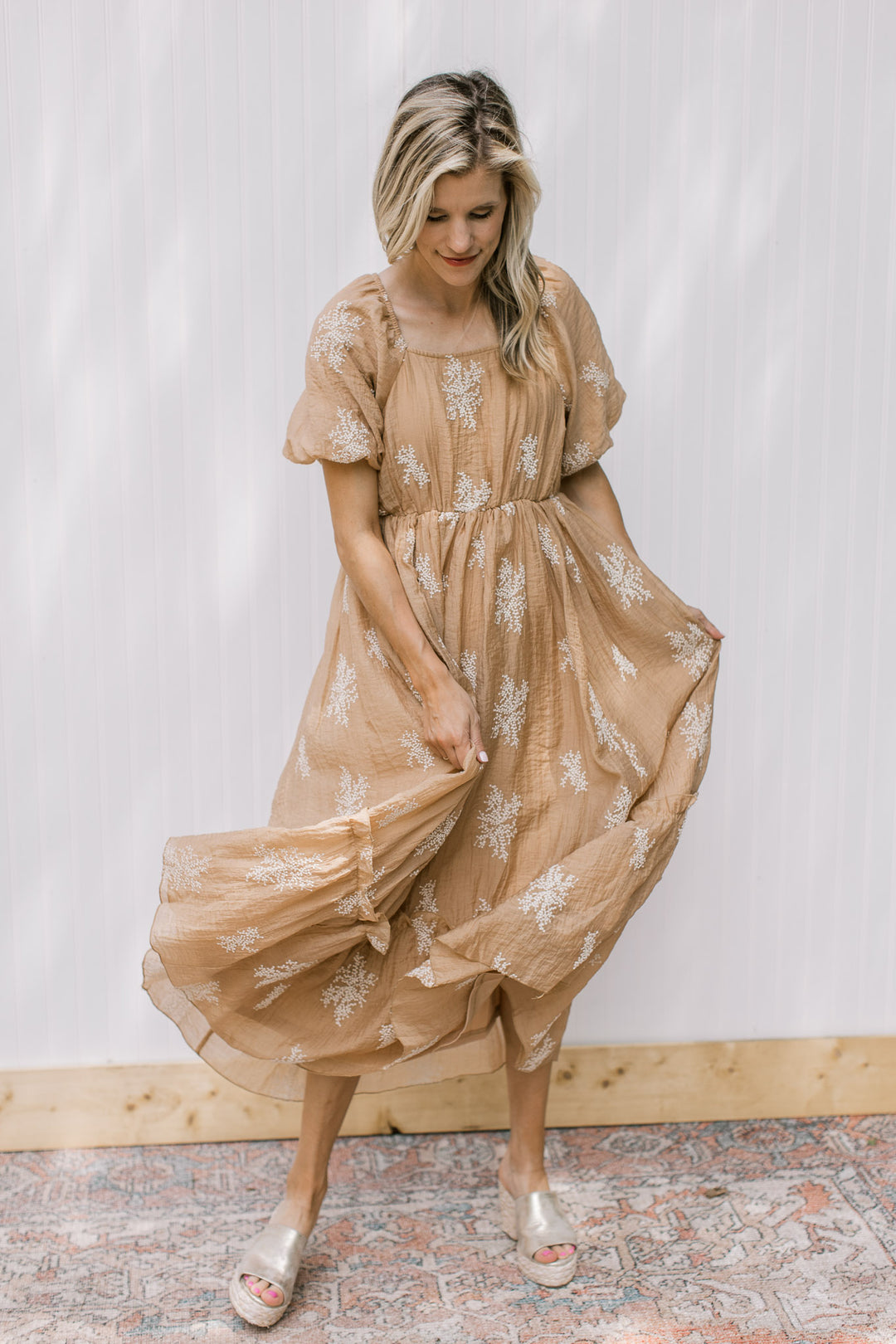 Model wearing a camel dress with white embroidered flowers, square neck and bubble short sleeves.