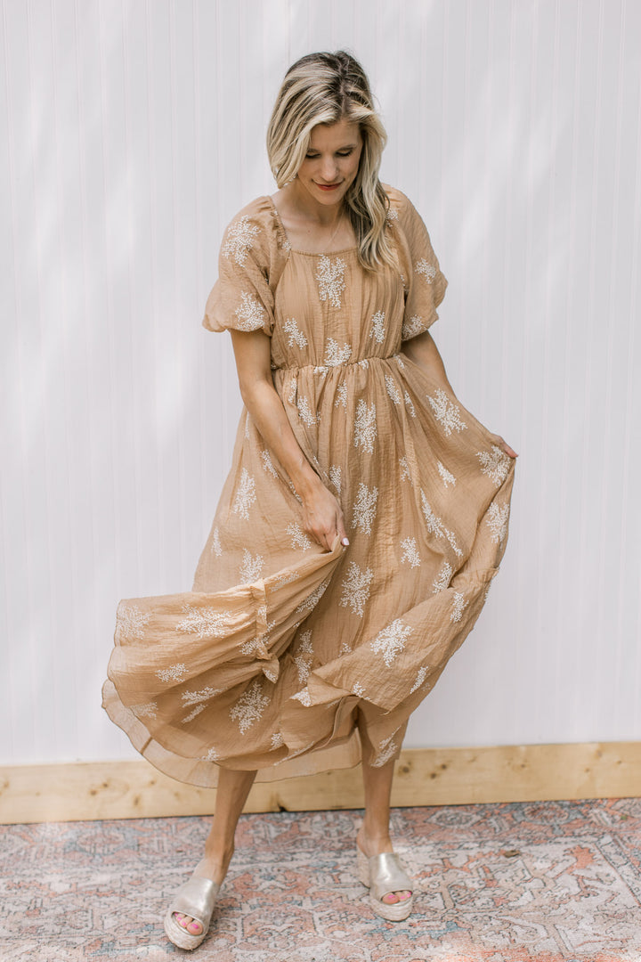 Model wearing a camel dress with white embroidered flowers, square neck and bubble short sleeves.