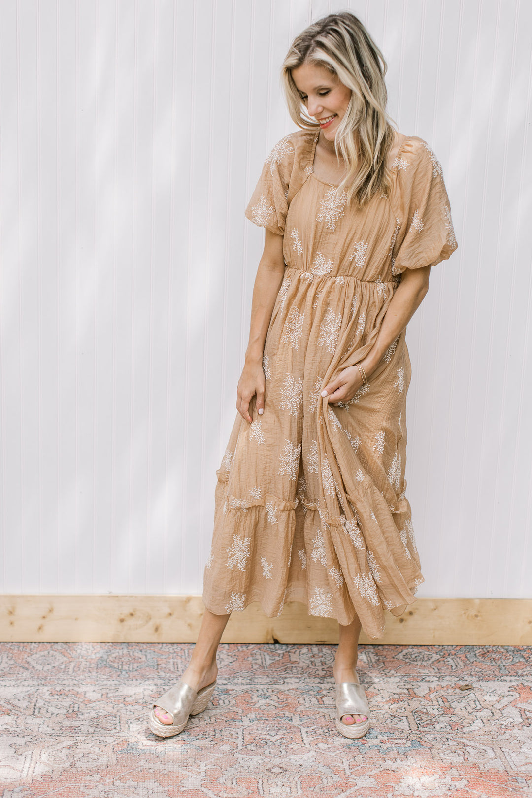 Model wearing a lined camel dress with white embroidered flowers and bubble short sleeves.
