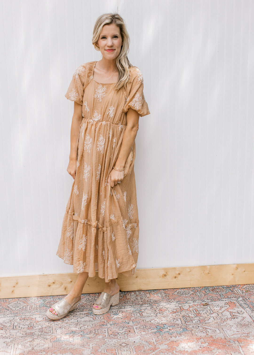 Model wearing a camel dress with white flower sprays, square neck and bubble short sleeves.