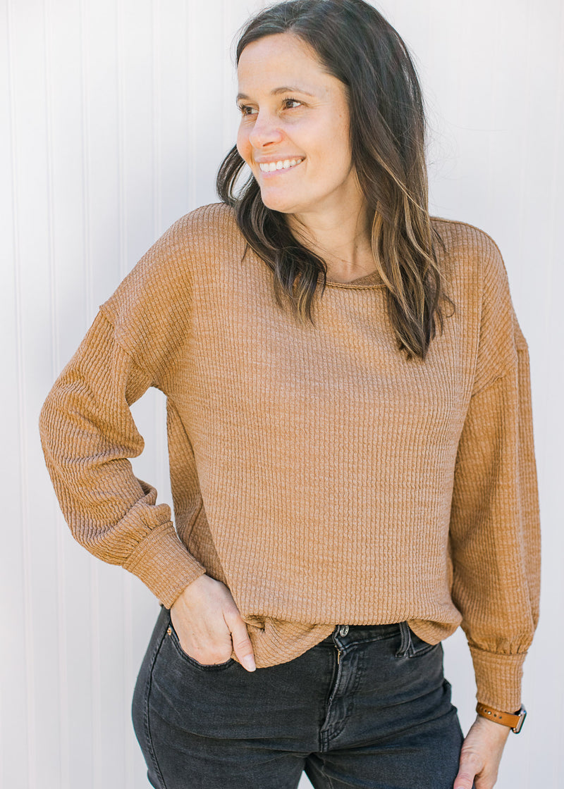 Model wearing a ribbed camel top with long sleeves, exposed hem and a round neck. 