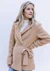 Model wearing a white top with a camel coat with long sleeves, a collard neck and side tie closure.