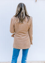 Back view of Model wearing a camel coat with long sleeves, a collard neck and a side tie closure. 