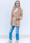 Model wearing jeans, mules and a white top with a camel long sleeve coat with  a side tie closure. 