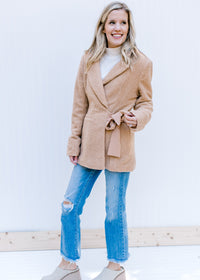 Model wearing jeans, mules and a white top with a camel long sleeve coat with  a side tie closure. 