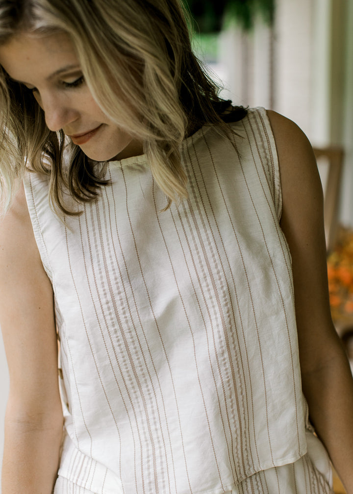 Close up of sleeveless, boatneck cream top with camel stripes, buttons at sides and a matching midi.