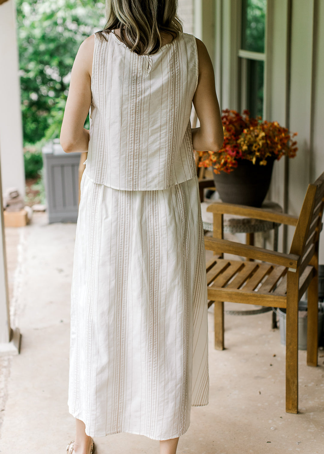 Back view of model wearing a cream set with camel stripes, sleeveless top and midi skirt bottom.