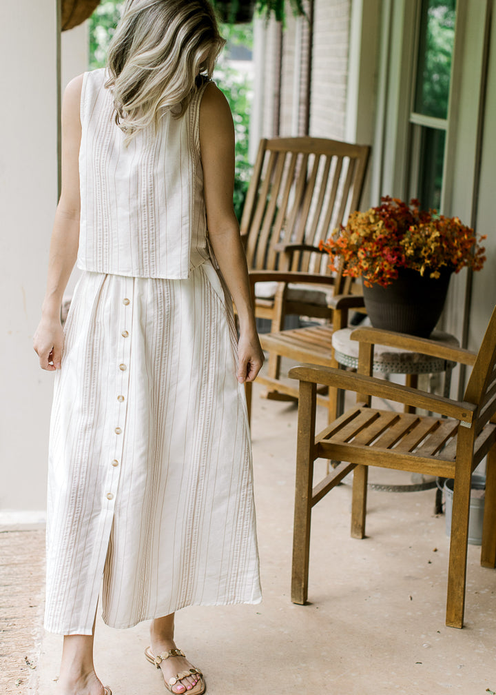 Model wearing sandals and a cream set with camel stripes button detail, sleeveless top and skirt.  