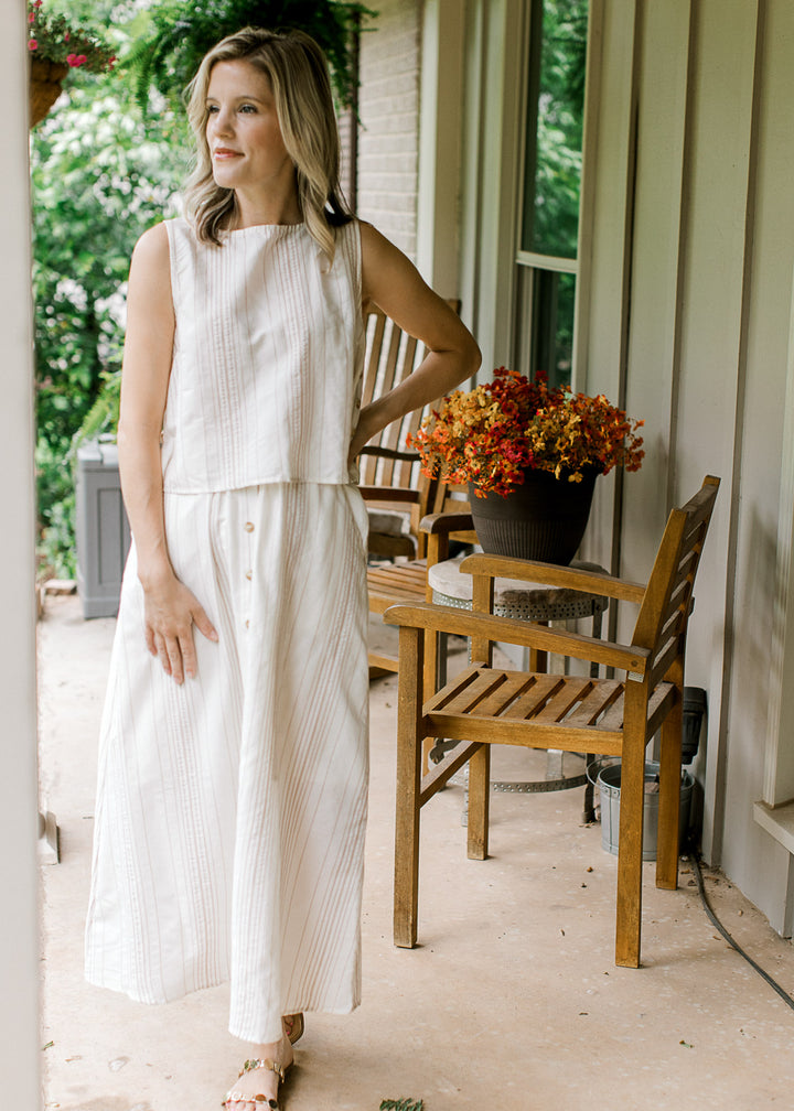 Model wearing a sleeveless cream top with a matching midi skirt with button front detail. 
