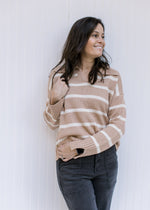 Model wearing a camel sweater with cream stripes, collar with a v-neck and split hem sleeve. 