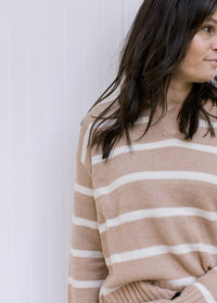 Close up view of a camel sweater with cream stripes, long sleeves and a v-neck with a collar. 