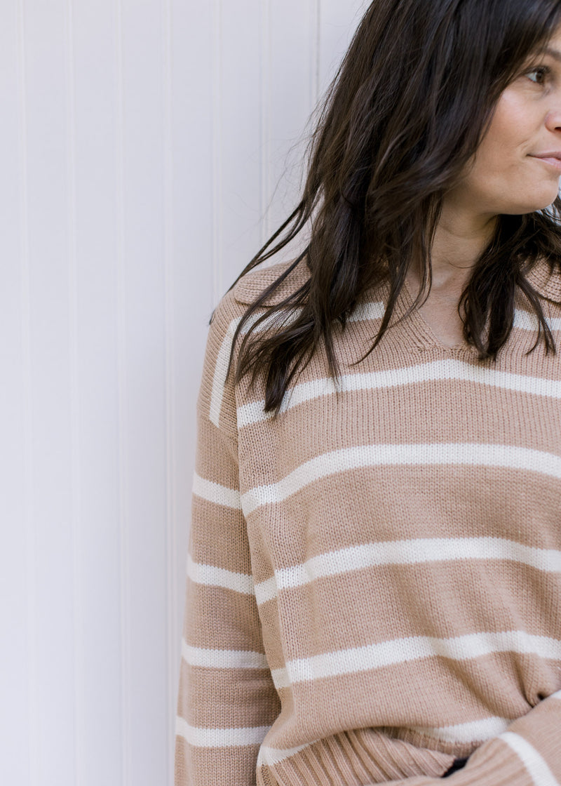 Close up view of a camel sweater with cream stripes, long sleeves and a v-neck with a collar. 