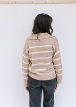Back view of a model wearing a camel sweater with cream stripes, long sleeves and a collared neck.