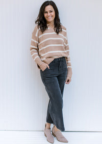 Model wearing jeans and booties and a camel sweater with cream stripes and split hem sleeve. 