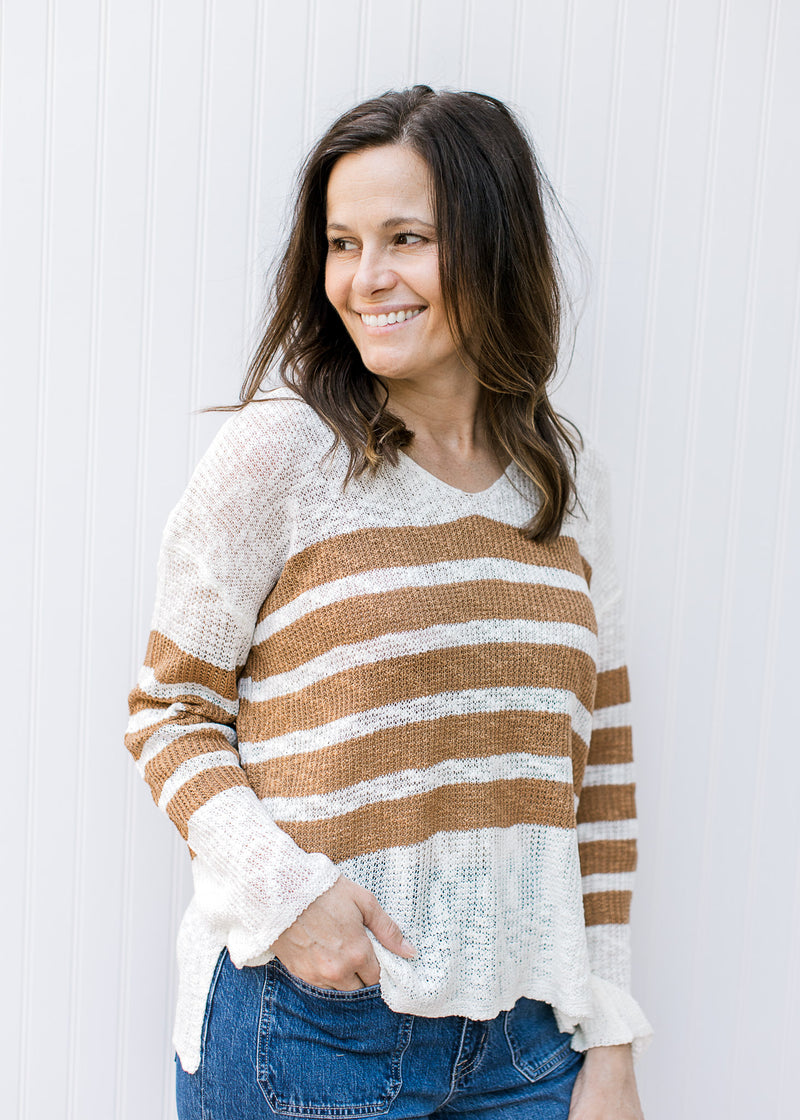 Model wearing jeans with a cream lightweight top with camel stripes, v-neck and long sleeves. 