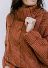 Close up of long sleeves and chunky cable knit design on a rust/camel colored sweater. 