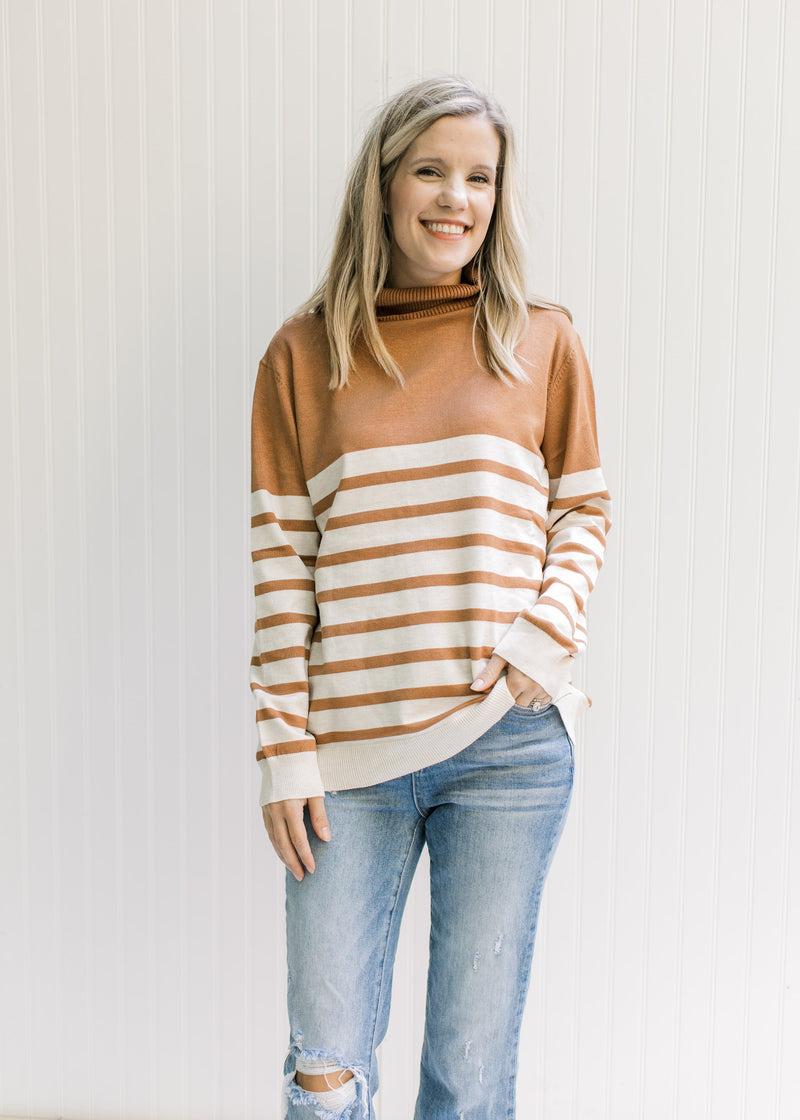 Model wearing a caramel and cream striped sweater with a turtleneck and long sleeves. 