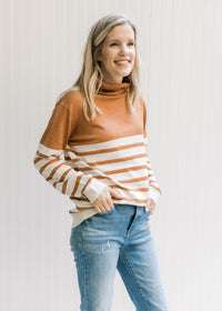 Model wearing jeans and a caramel and cream striped sweater with a turtleneck and long sleeves. 