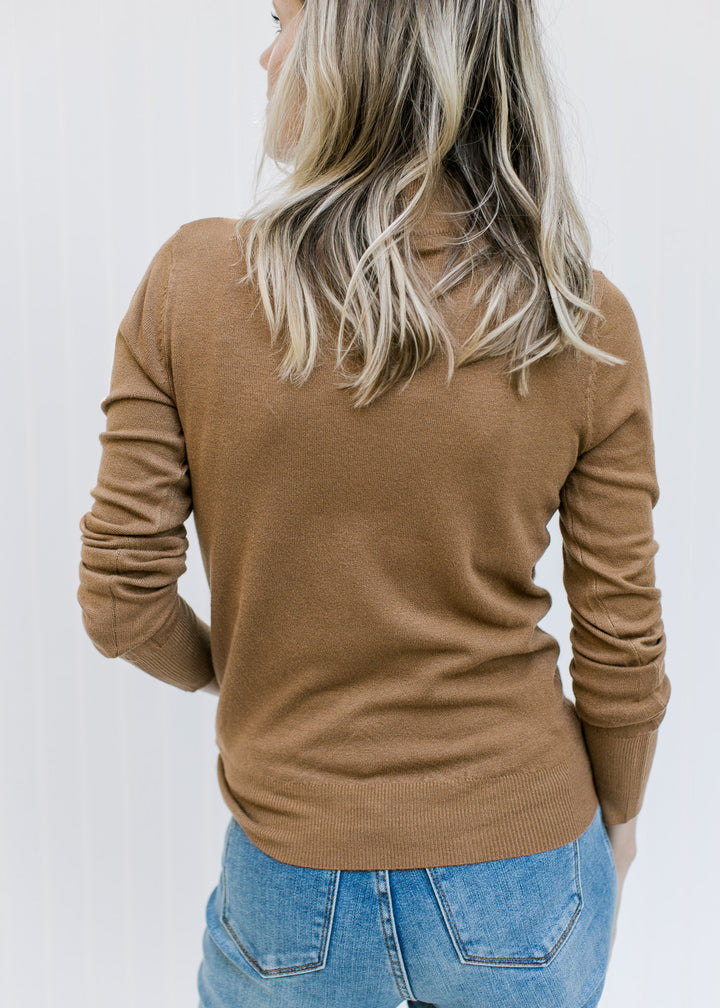 Back view of Model wearing a lightweight caramel knit top with long sleeves and a mock neck. 